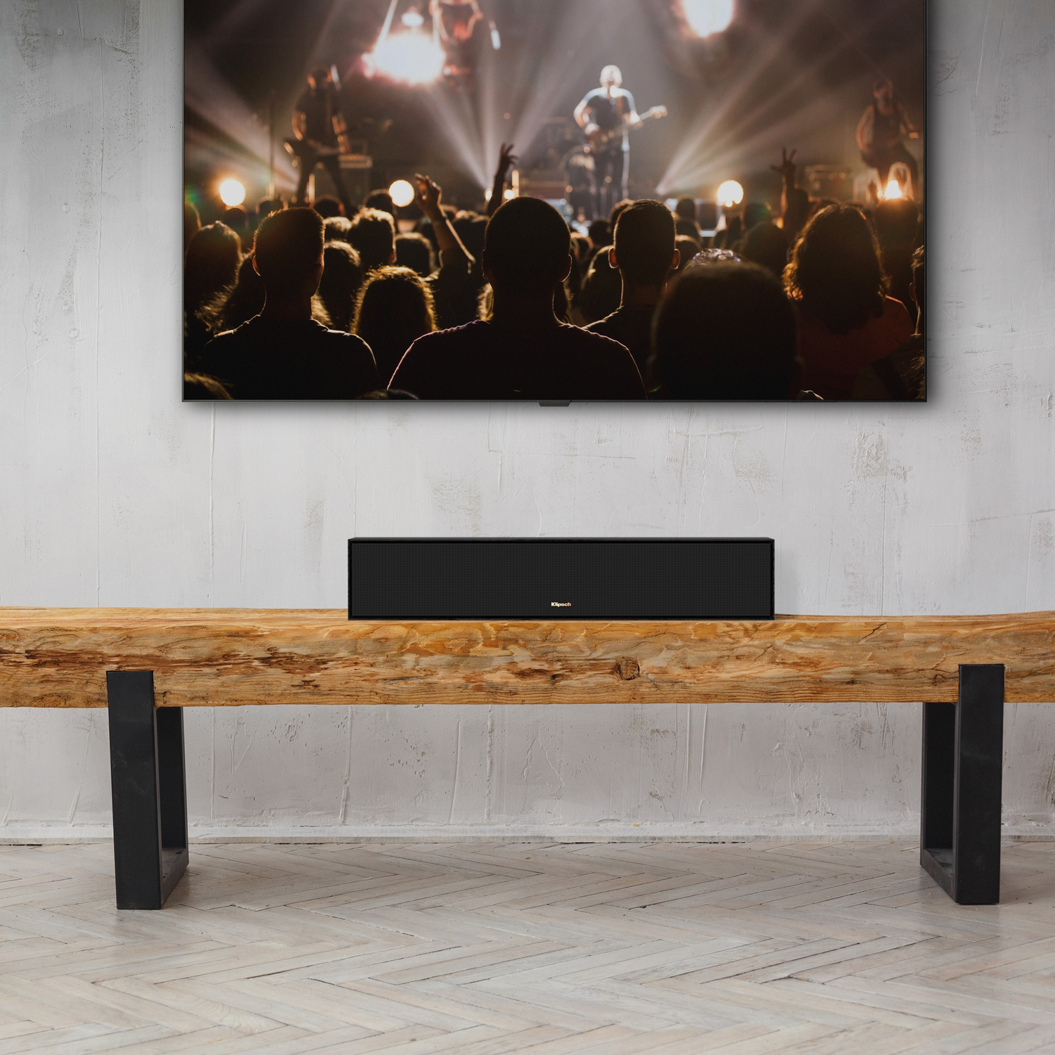 Een woonkamer met een tv boven een soundbar op een houten bank, mensen in silhouet op de achtergrond.