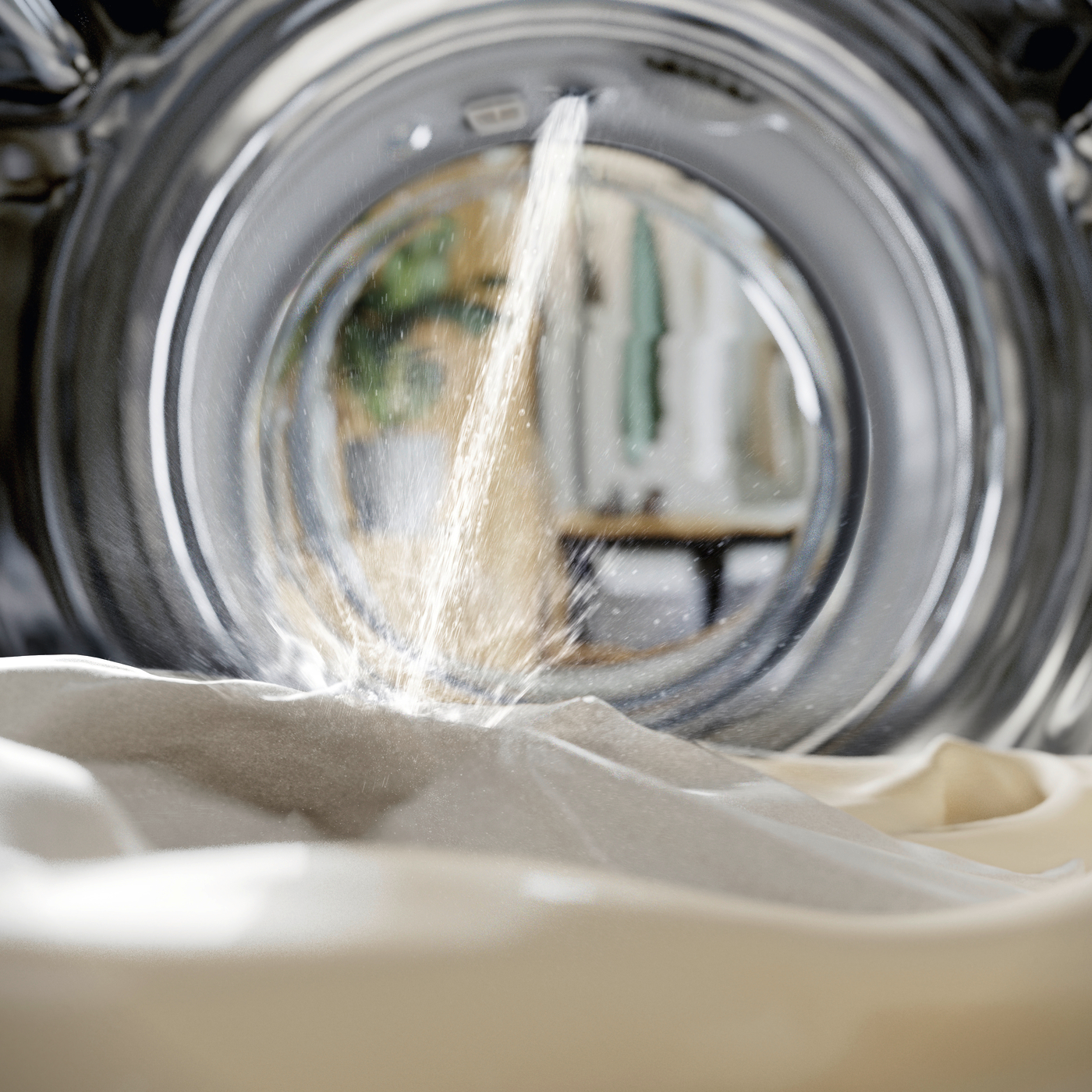 Tambour de machine à laver avec de l'eau et des vêtements. L'eau coule sur les vêtements.