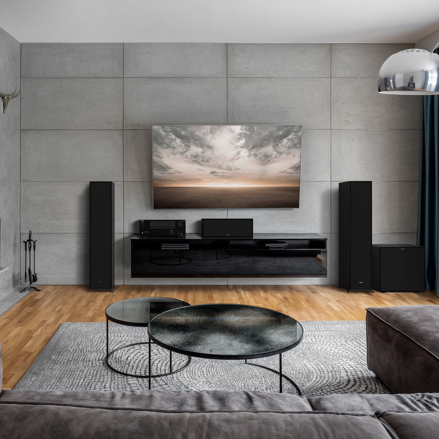 Modern living room with gray couch, TV, speakers, and coffee tables.