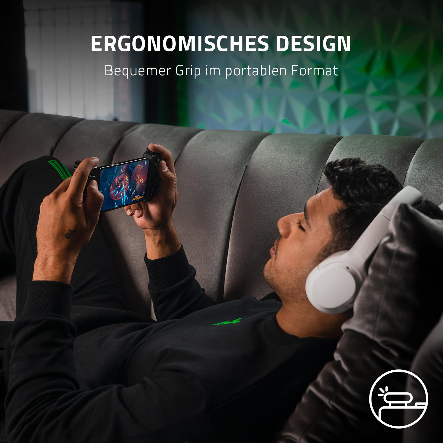 Mann spielt auf einem Handy mit Gamepad, trägt Kopfhörer, auf einem Sofa.