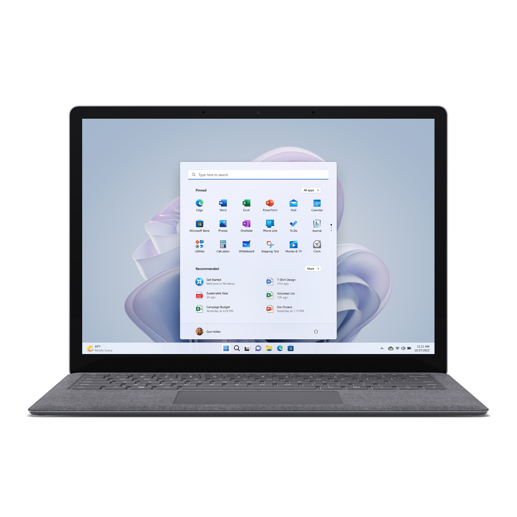 Una laptop gris abierta sobre una mesa. La pantalla muestra la pantalla de inicio de Windows 11.