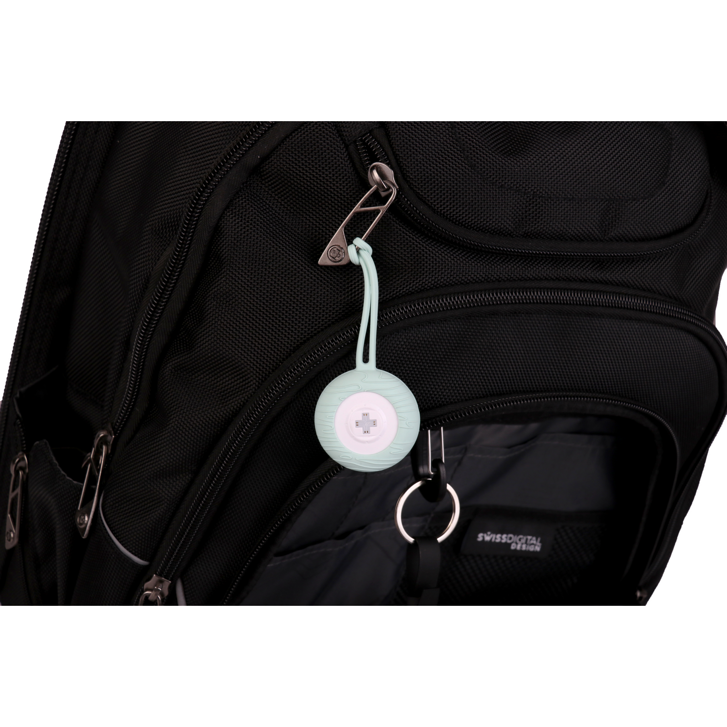 A mint green speaker hanging from a black backpack with a Swissdigital Design label on it.