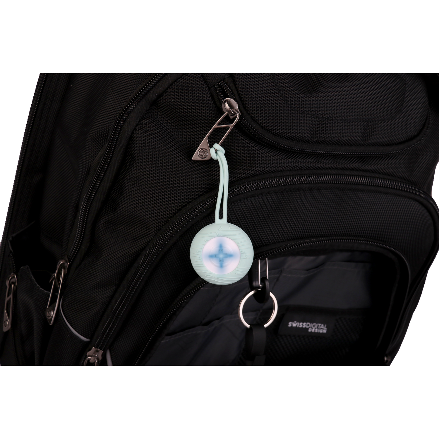 A light blue circular object with a strap is hanging on a backpack.  It features a pattern.