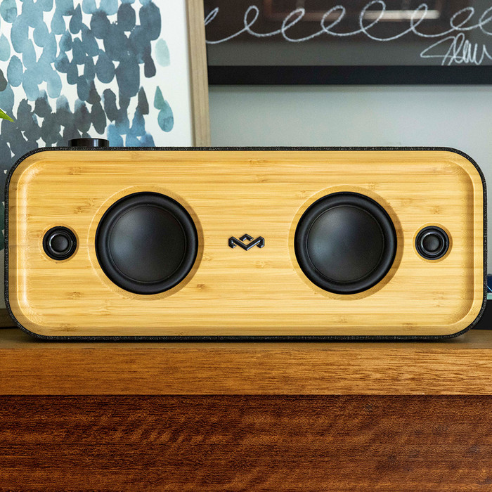 A wooden speaker with two black speakers, and a logo in the middle, on a wooden table.