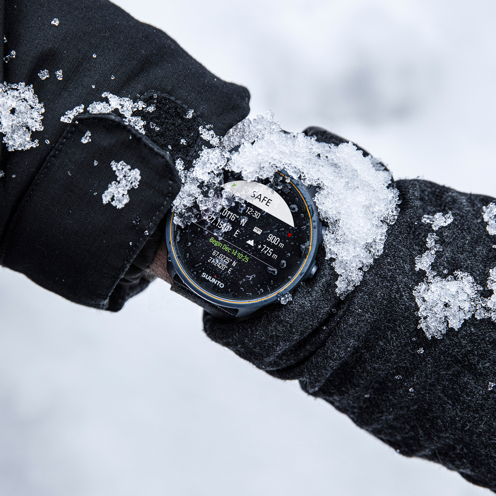 Person mit Handschuhen, die eine mit Schnee bedeckte Smartwatch überprüft, verschneiter Hintergrund.