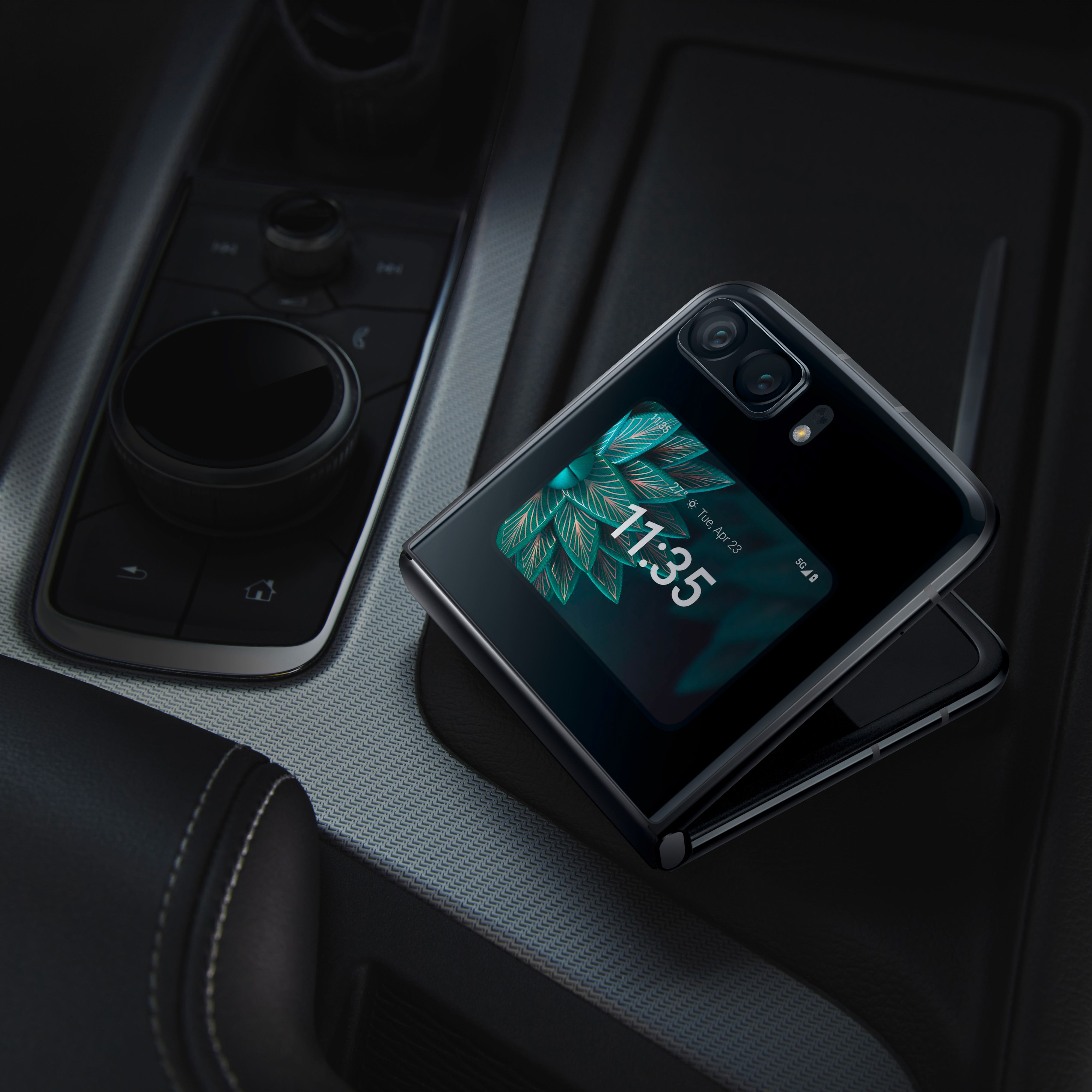 Faltbares schwarzes Smartphone auf einer Autokonsole, Bildschirm zeigt Zeit und Blätter.