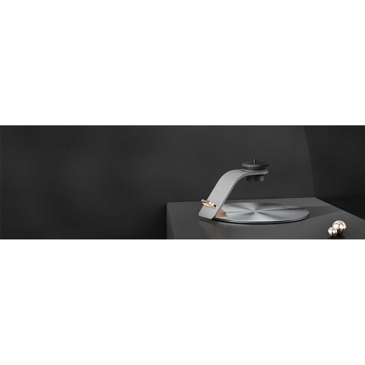 A silver and gold monitor stand on a dark surface. Background is black.