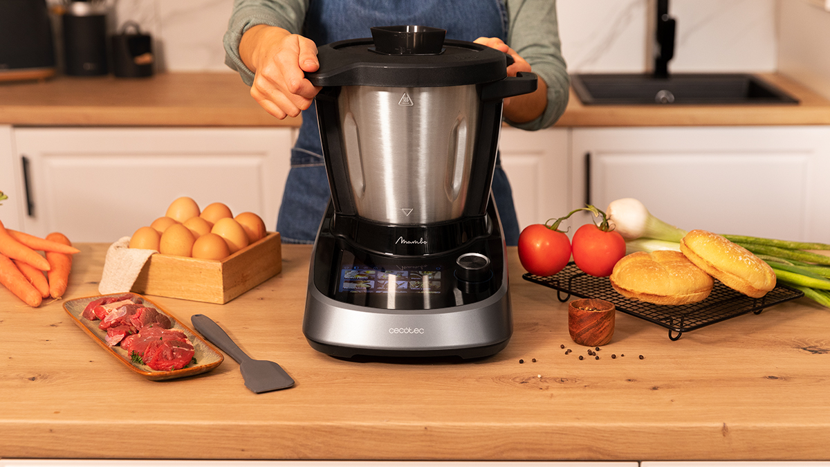 Una mujer usando un electrodoméstico de cocina. Ingredientes como verduras y huevos en la mesa.