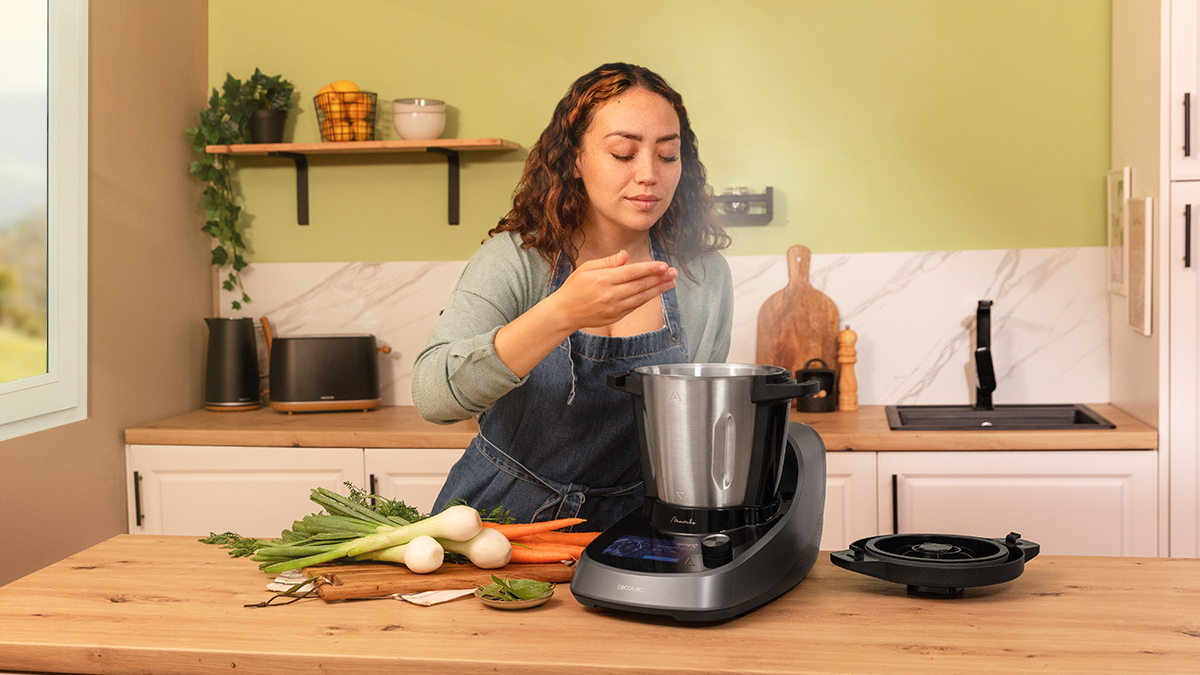 Mujer en cocina, huele comida de máquina, verduras en la mesa.