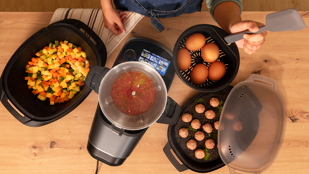 Una persona cocinando. Varios alimentos en recipientes, incluyendo verduras picadas y albóndigas.