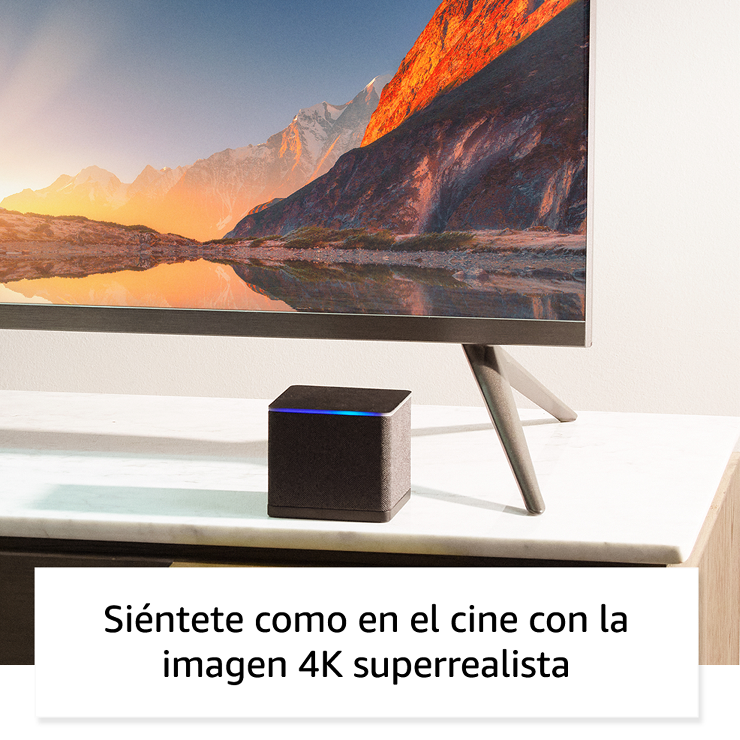 Un altavoz negro sobre una mesa blanca con un televisor al fondo. El texto dice 'Siéntete como en el cine'.