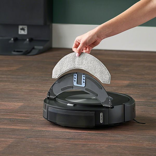 Eine Hand legt ein Reinigungspad auf einen schwarzen Roboter-Staubsauger.