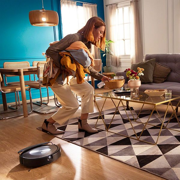 Frau trägt Kleidung und legt sie auf einen Tisch, mit einem Roboter-Staubsauger auf dem Boden.