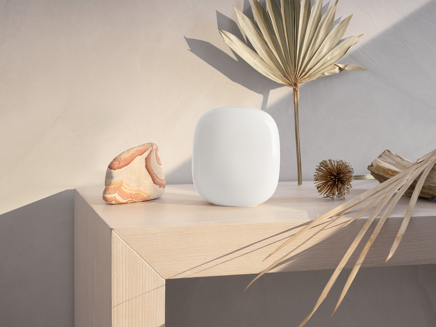 Een wit smart home apparaat op een houten tafel met een steen en een palmblad. Beige muur op de achtergrond.
