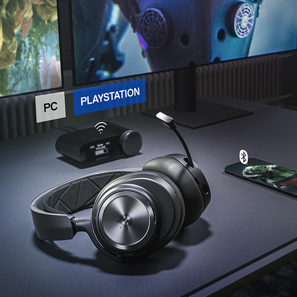 Black gaming headset with a microphone, set up on a desk with a phone and a display.