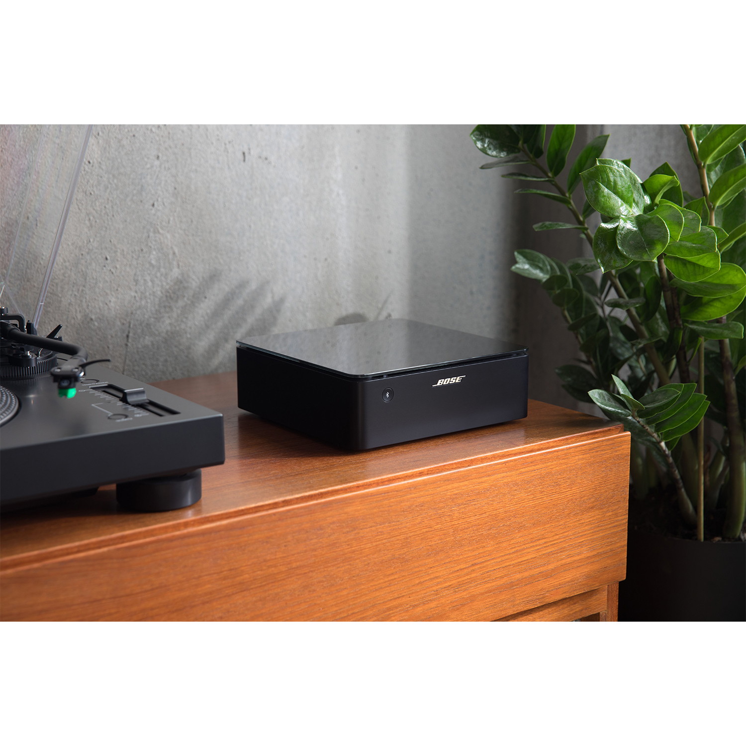 Un sistema audio Bose nero su una superficie di legno accanto a un giradischi nero e una pianta.