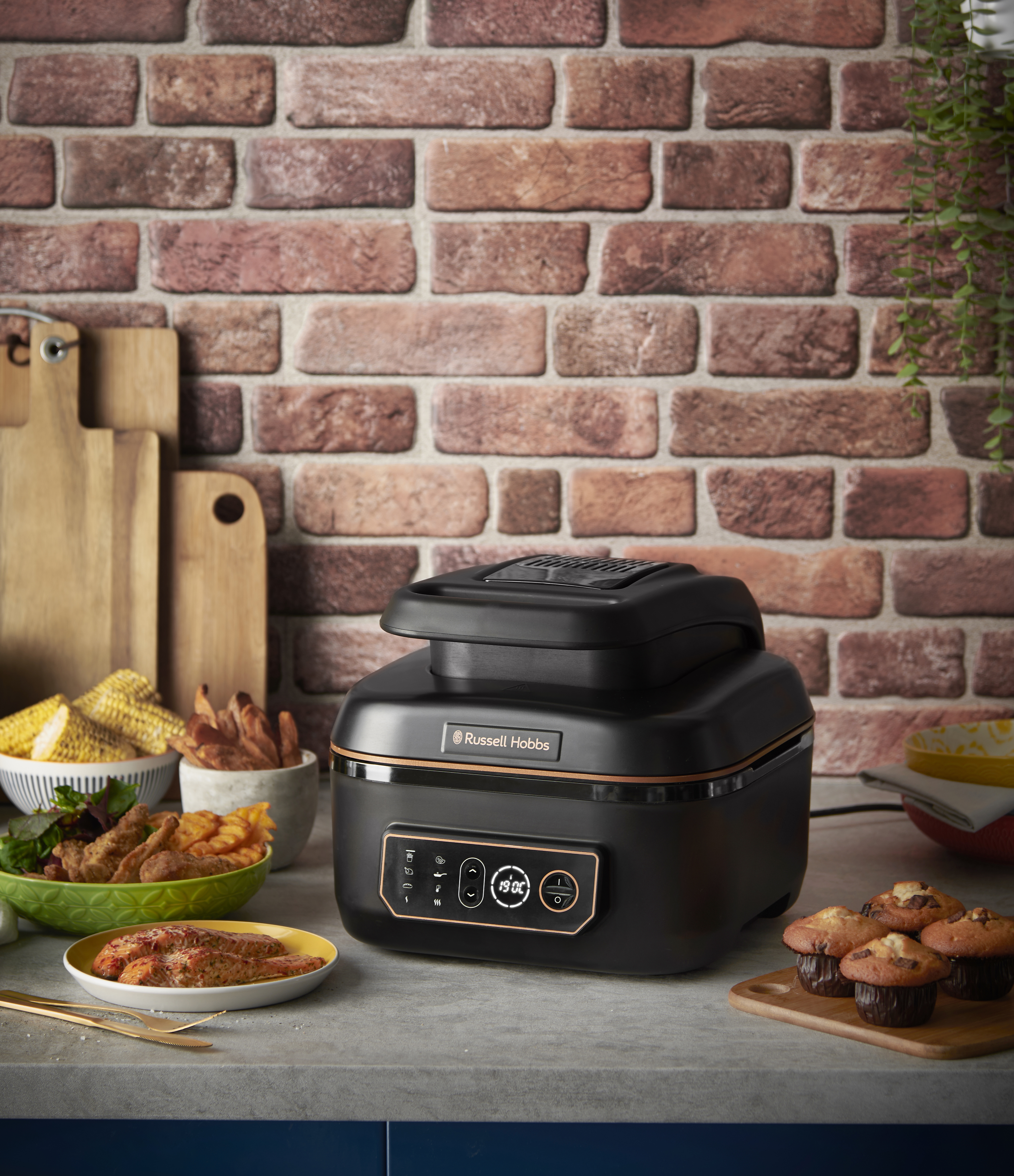 Fekete Russell Hobbs légkeveréses sütő étellel, téglahátfallal, muffinokkal, sült krumplival és csővel.