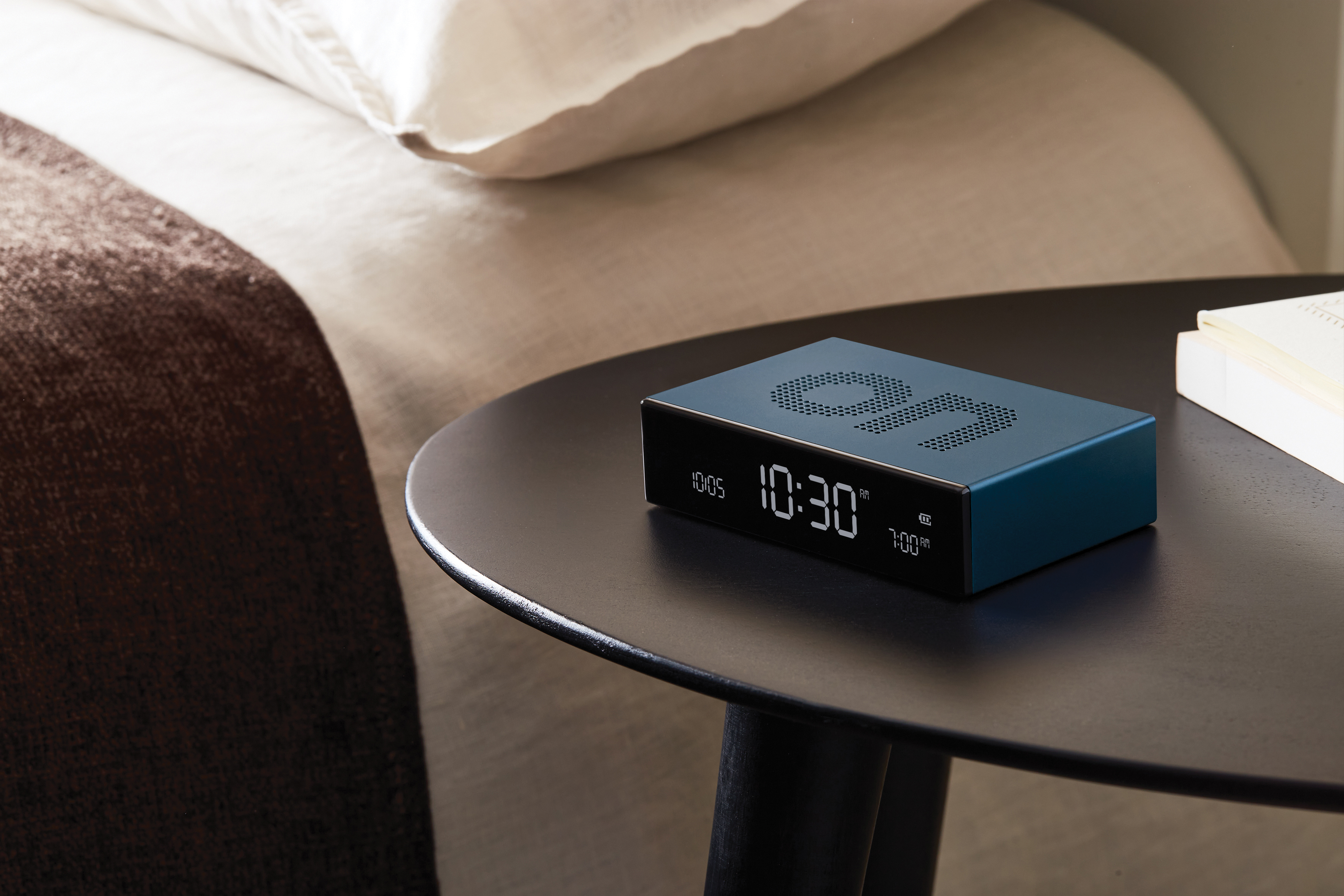 Una sveglia blu su un tavolo nero accanto a un letto. L'ora visualizzata è 10:30.