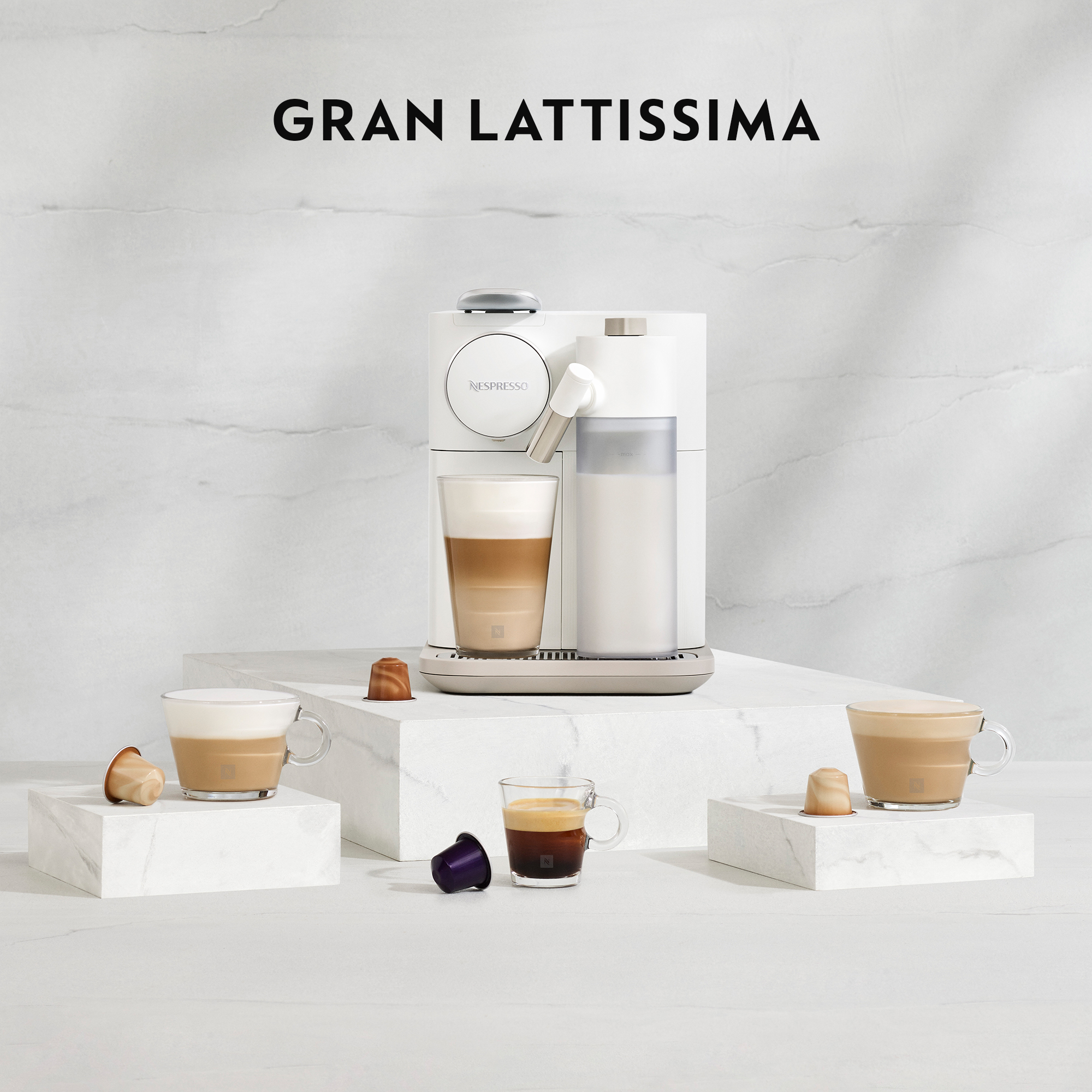 Machine Nespresso blanche avec tasses et dosettes sur plateforme blanche.