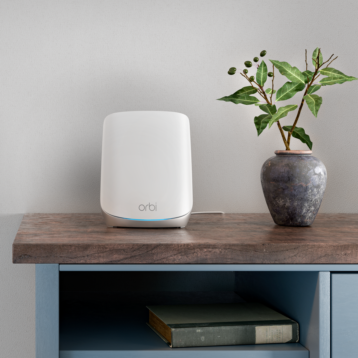 White Orbi router on a wooden table, next to a vase with green plant.