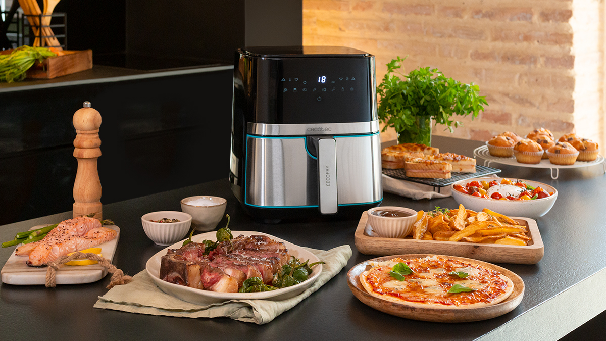Freidora de aire con comida en la encimera: bistec, pizza, papas fritas, magdalenas y verduras.