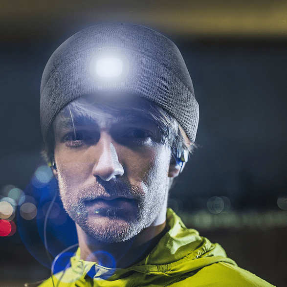 Un homme portant un bonnet gris avec une lumière intégrée, dans un environnement sombre.