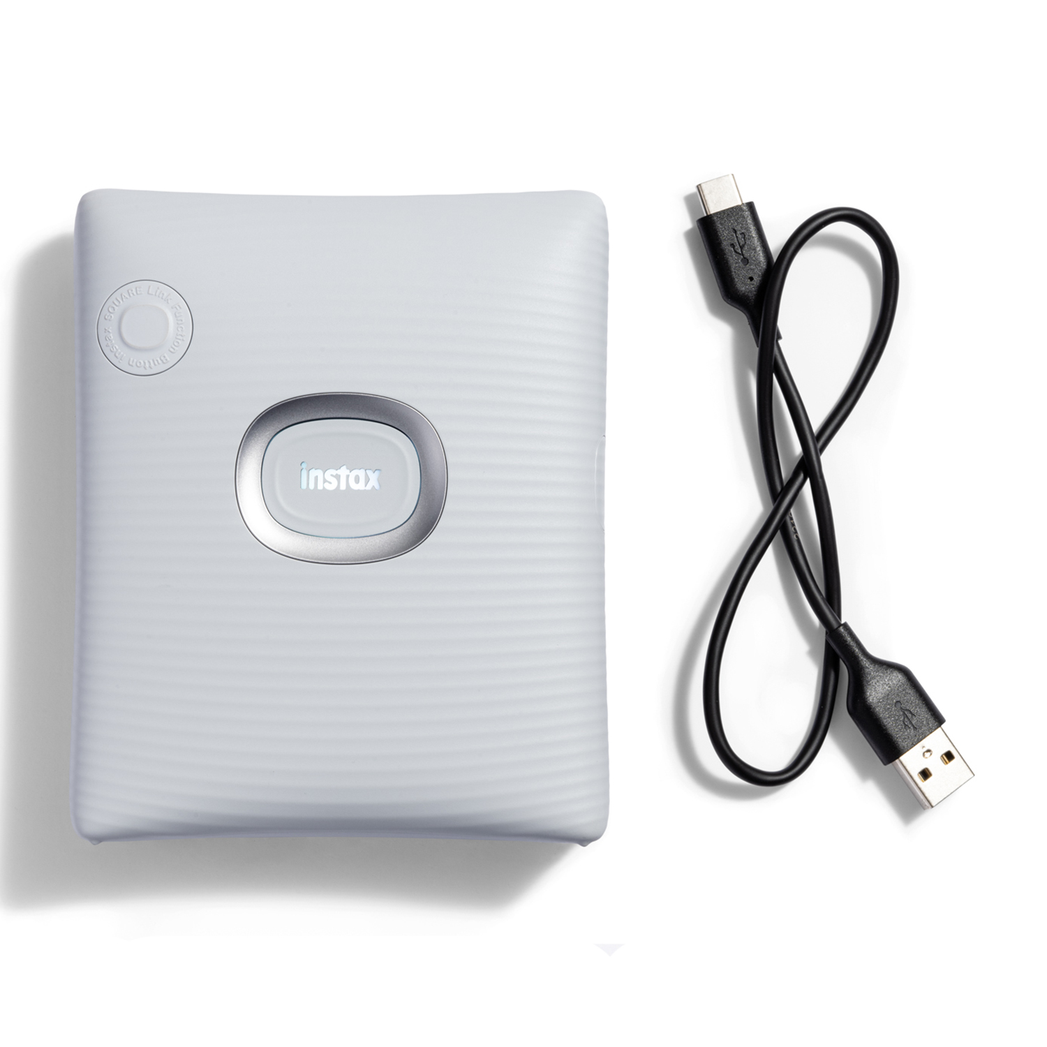 Una stampante Instax bianca con un cavo USB nero. Il dispositivo ha un pulsante ovale centrato.