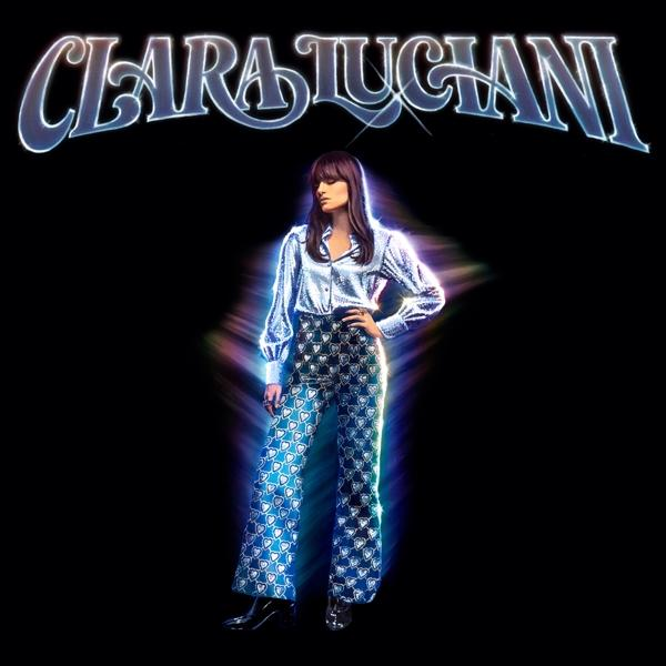 Pochette d'album de Clara Luciani. Elle porte une chemise argentée scintillante et un pantalon à motifs. Fond noir.