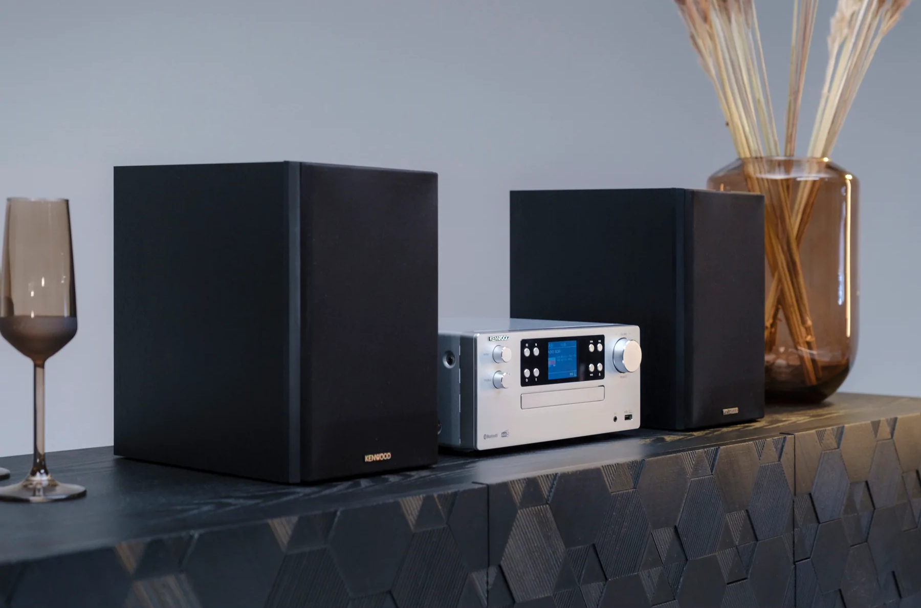 Impianto stereo su un mobile nero. Include due altoparlanti, un ricevitore e oggetti decorativi.