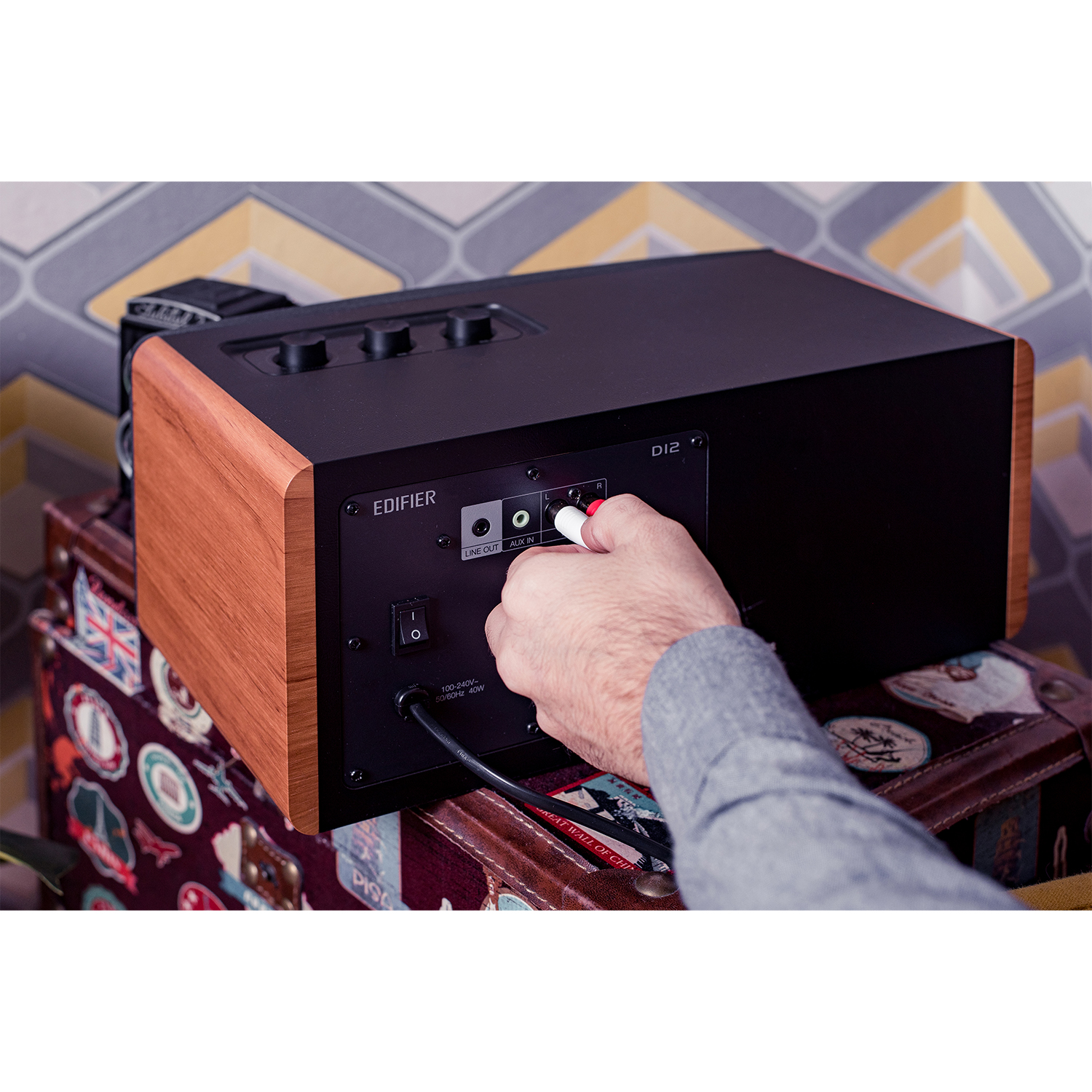 Una persona collega un cavo RCA rosso e bianco al retro di un altoparlante nero e legno.