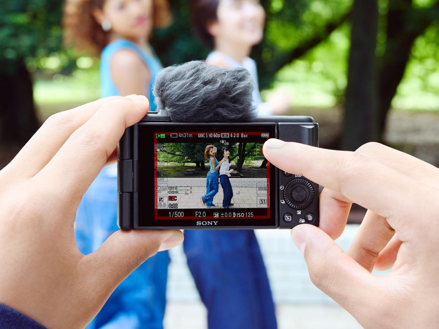 Persona sosteniendo una cámara filmando a dos mujeres en un parque. La pantalla es visible.