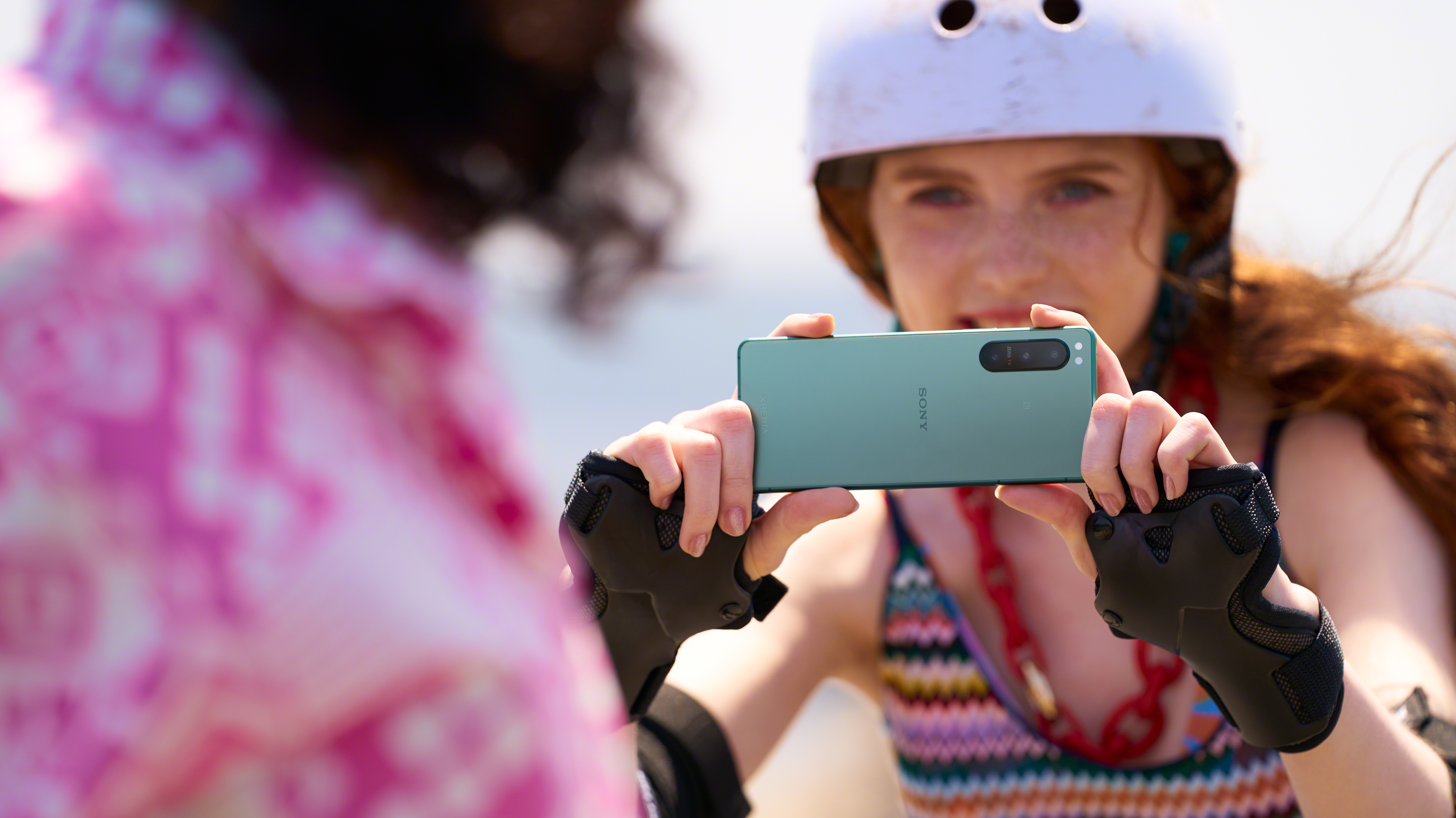 Eine Frau hält ein grünes Telefon und macht ein Foto von einer Person in rosa Top und Helm.