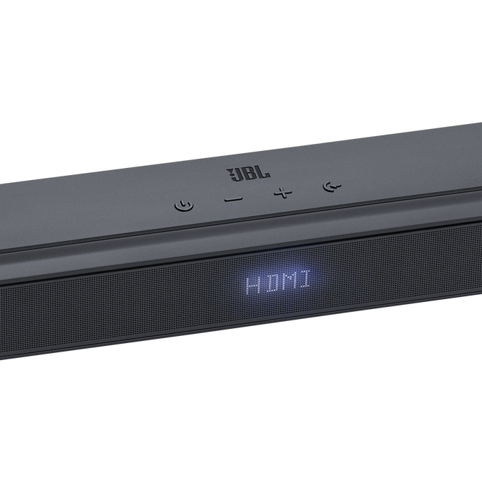 Barra de sonido JBL, negra, mostrando 'HDMI'. Controles en la parte superior. Fondo negro.