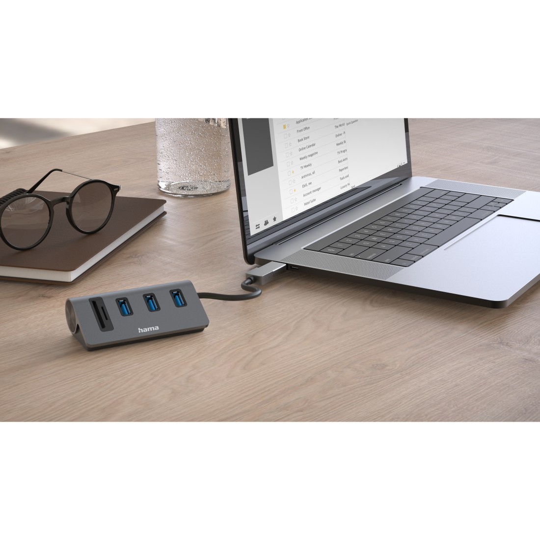 Laptop mit USB-Hub auf einem Holztisch. Brille und Notizbuch sind sichtbar.