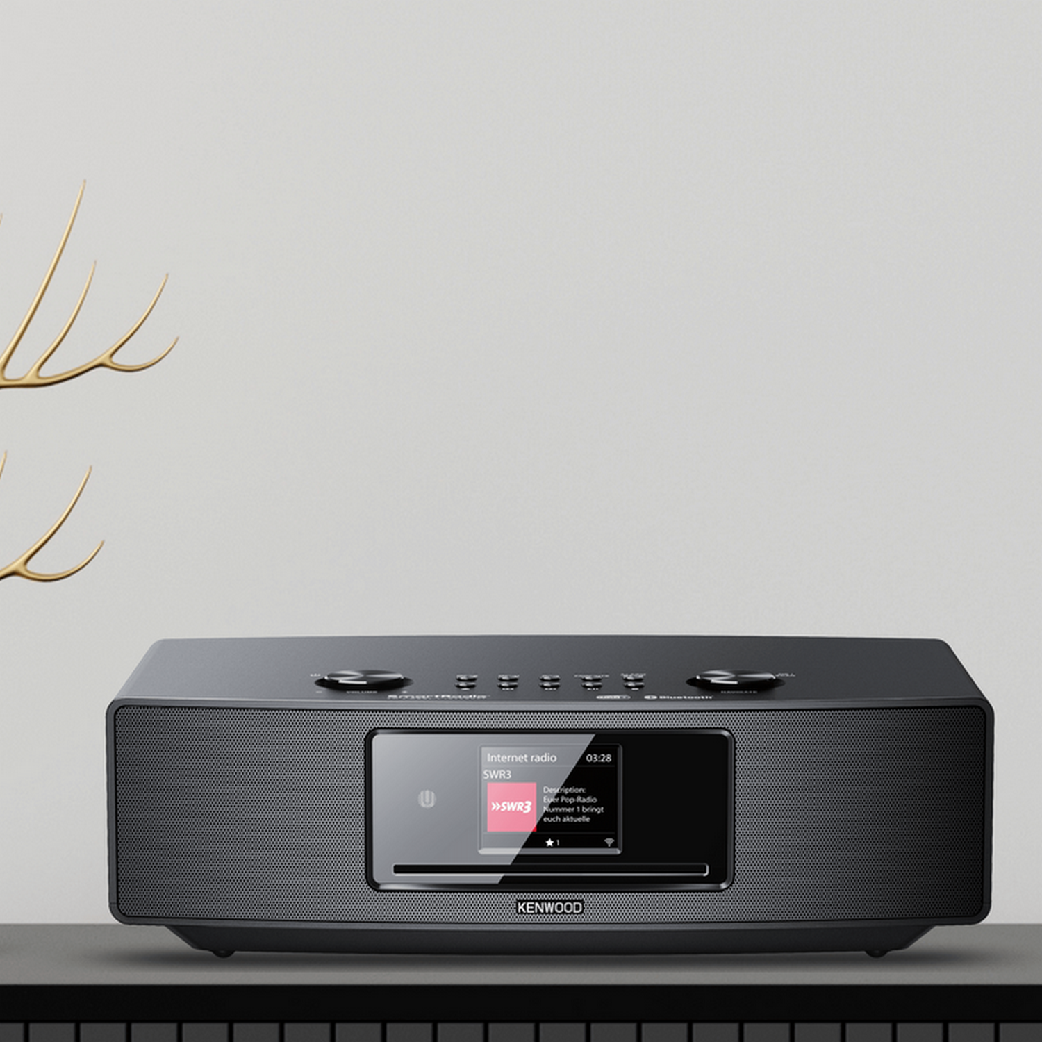 A black Kenwood internet radio with a screen. Gold decorative object on top.