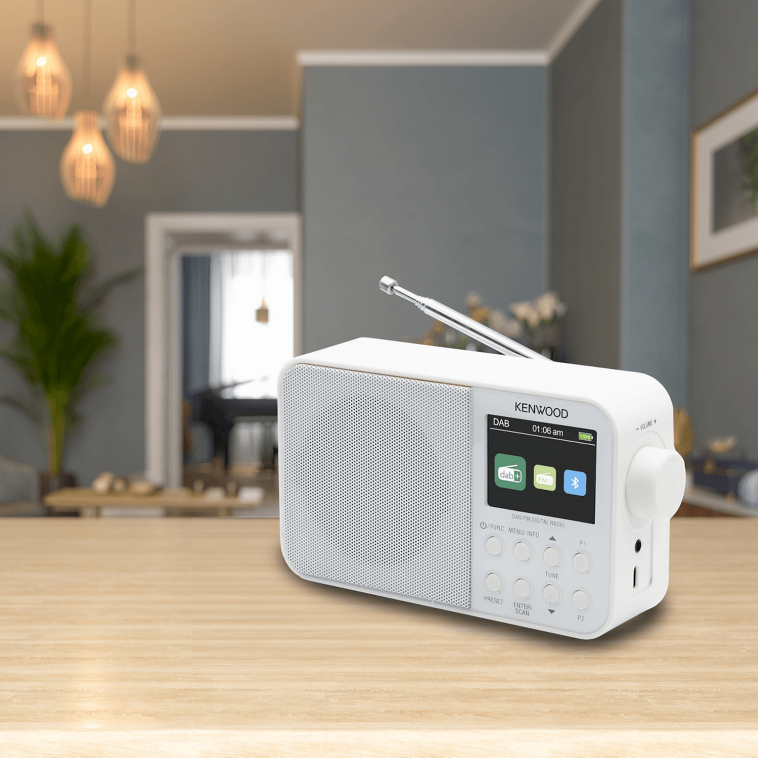 Een witte Kenwood radio op een houten tafel, met een wazige woonkamer op de achtergrond.