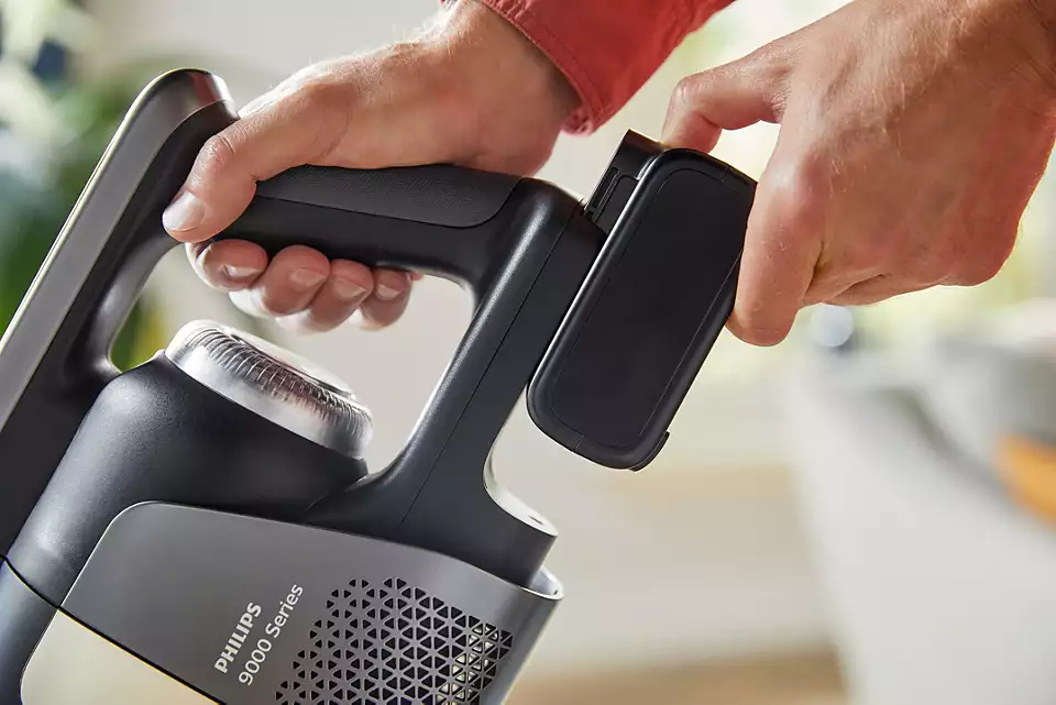 Hände setzen einen Akku in einen schwarzen und grauen Philips Staubsauger ein. Der Hintergrund ist unscharf.