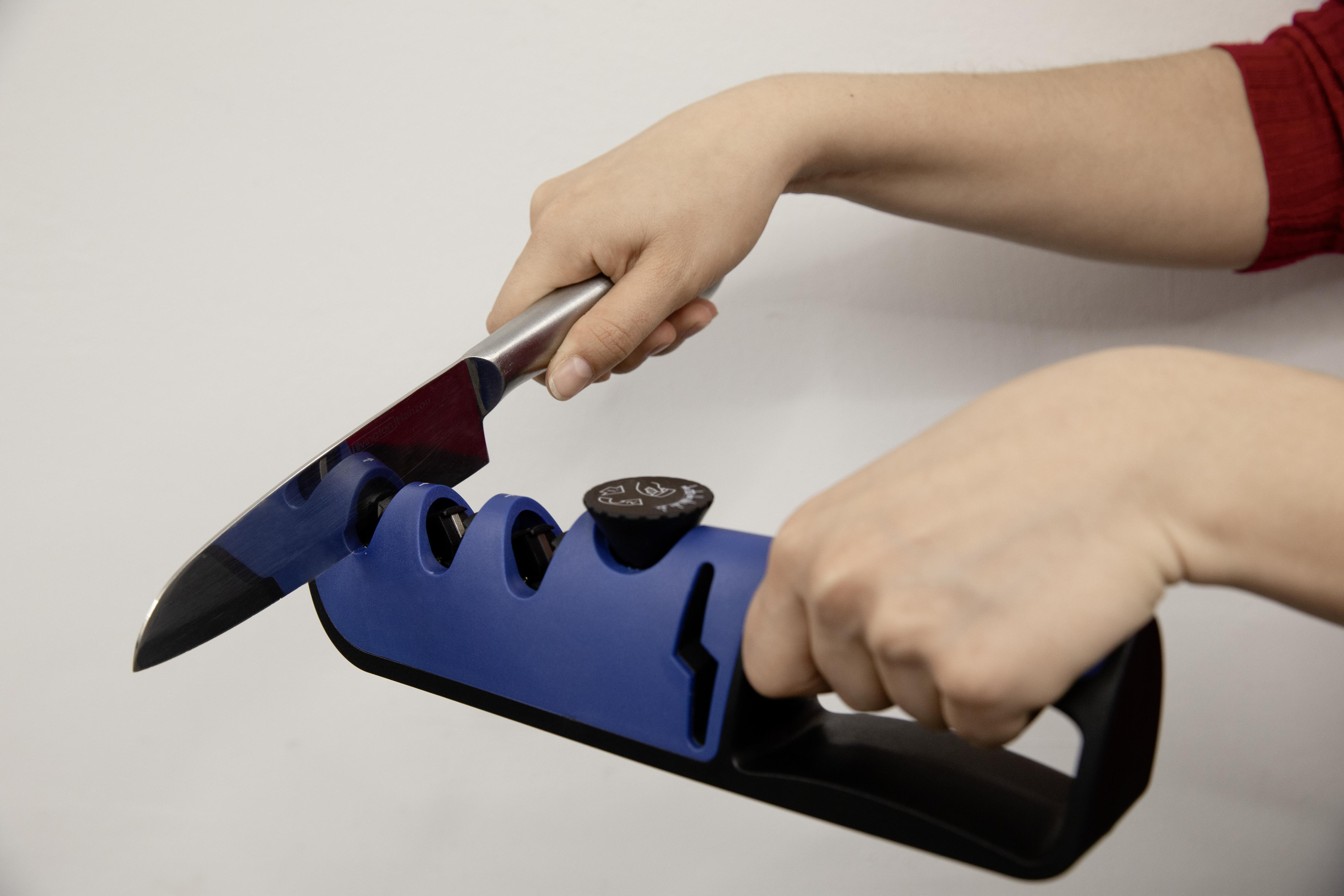 Hände, die ein Messer mit einem blauen Messerschärfer schärfen. Weißer Hintergrund.