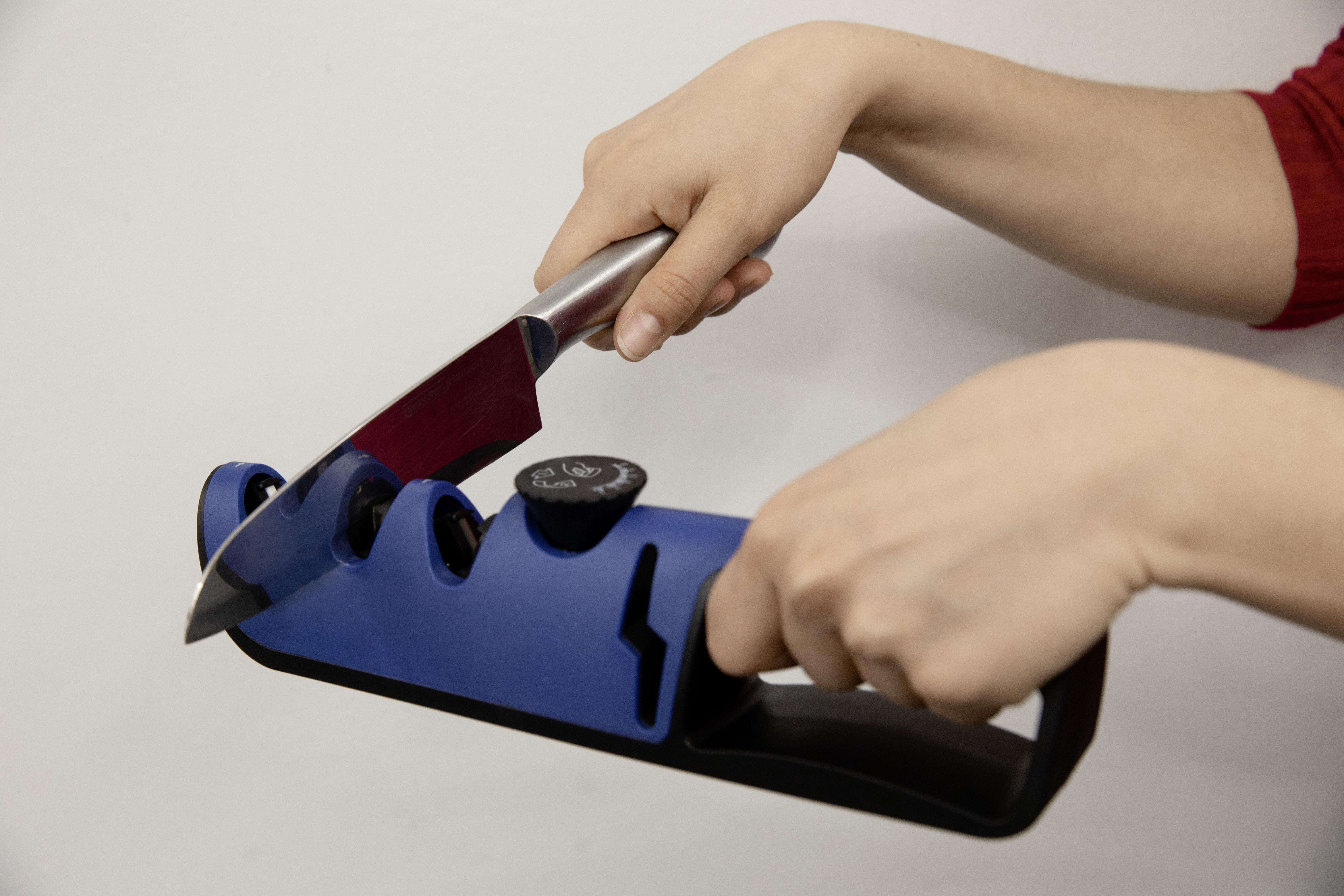 Hände schärfen ein Messer mit einem blauen Messerschärfer vor weißem Hintergrund.