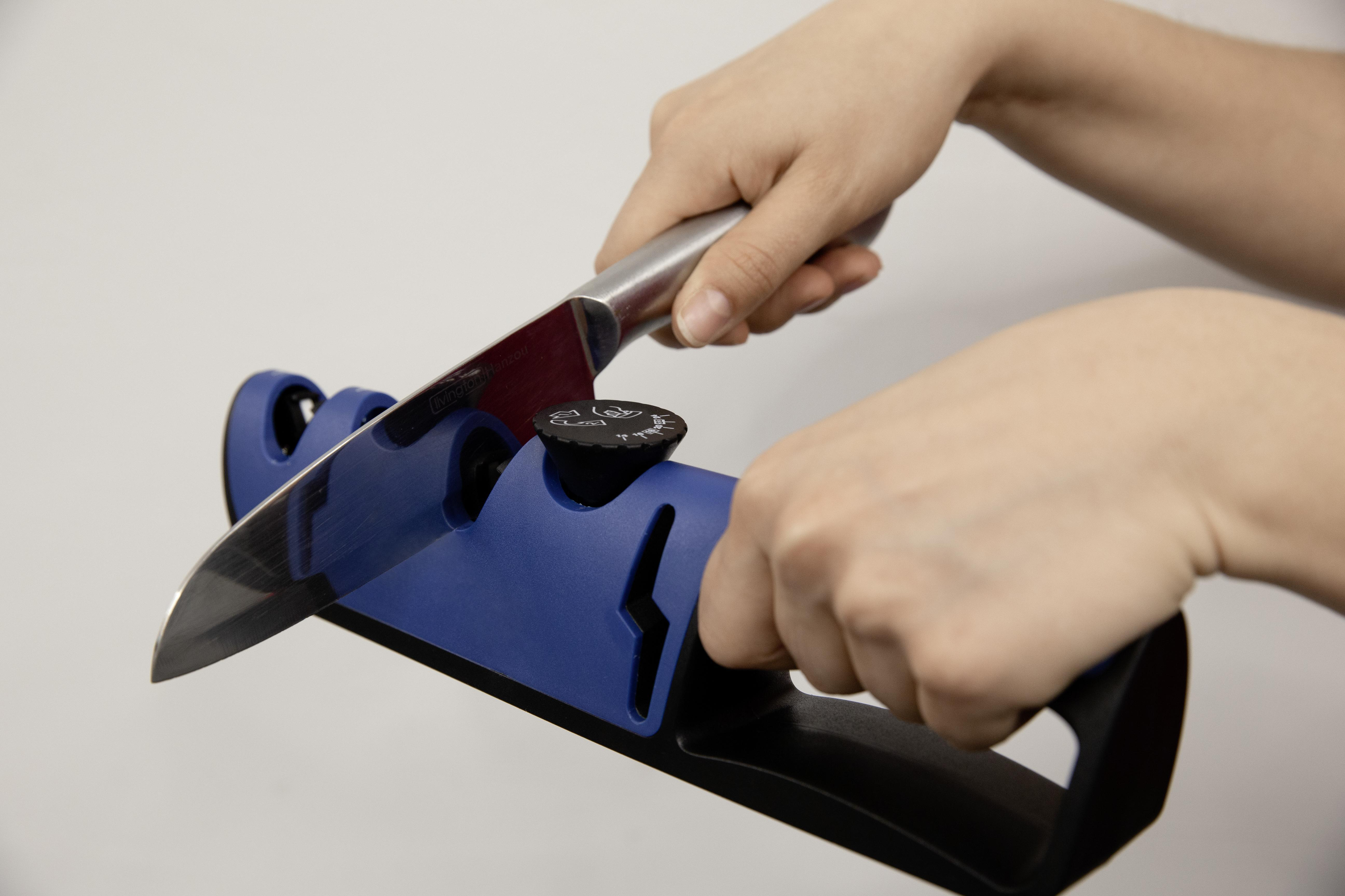 Hände schärfen ein Messer mit einem blau-schwarzen Schärfer.