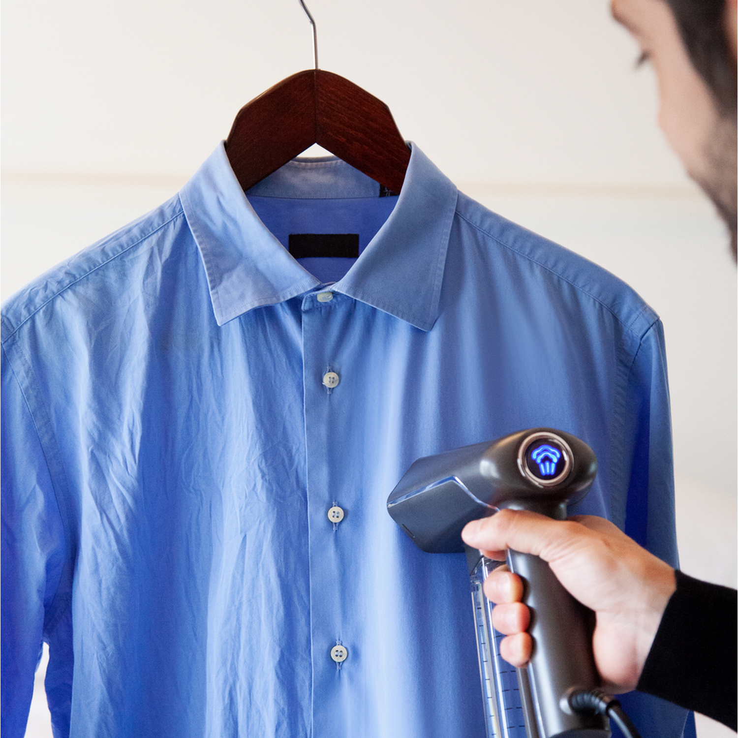 Persoon stoomt een blauw overhemd op een houten hanger met een handstomer.