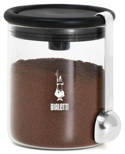 Glasbehälter mit Kaffeepulver und silberner Schaufel. Schwarzer Deckel. Weißer Hintergrund.