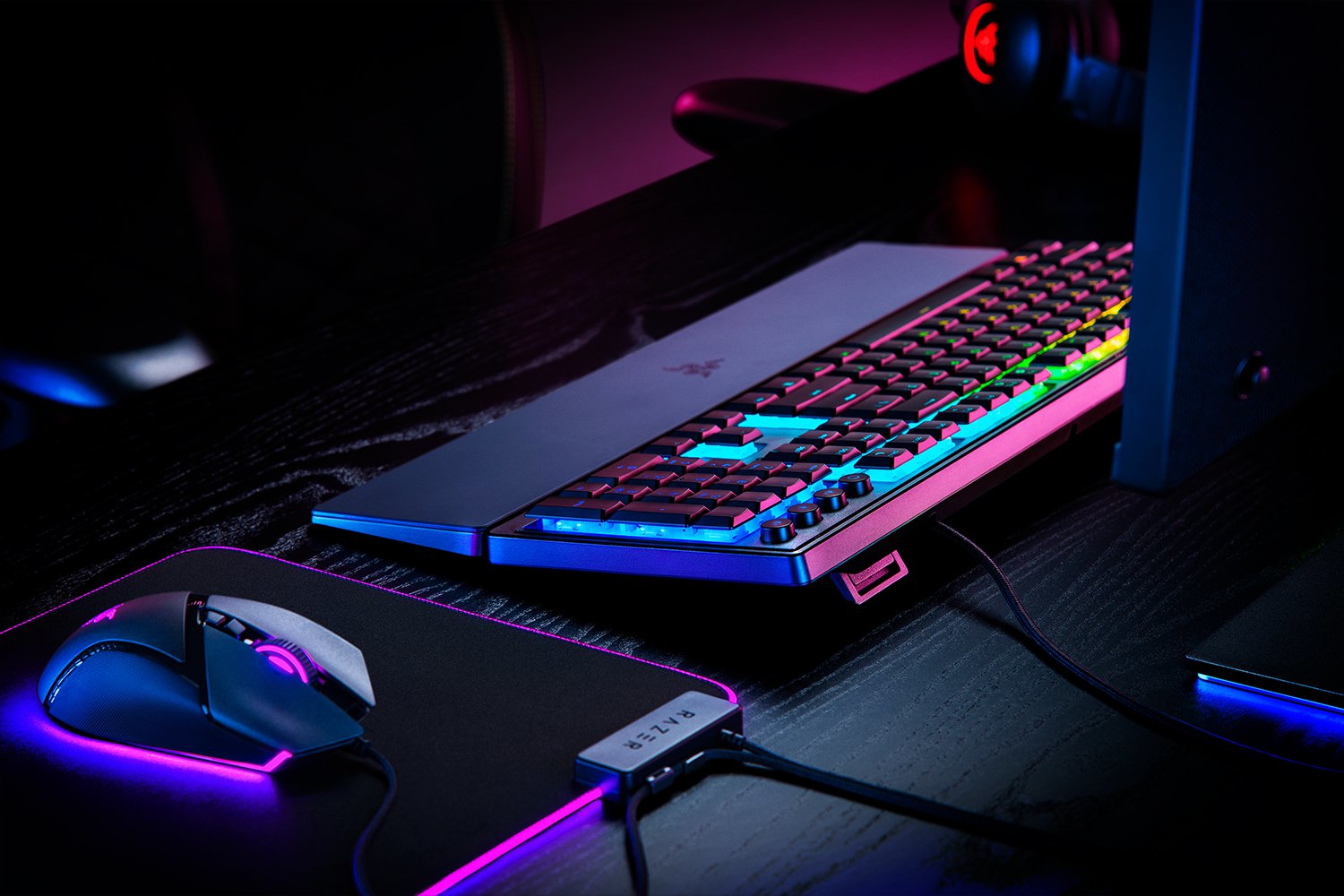 Gaming setup with a Razer keyboard and mouse. Keyboard has colorful lights. Black desk.