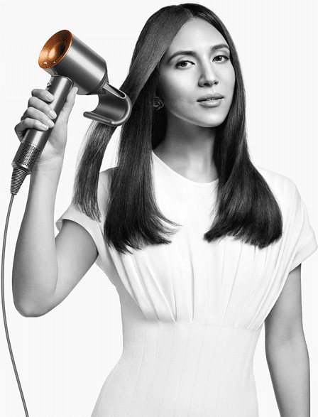 A woman is using a hair dryer, blowing air on her hair. It is a black and white photo.