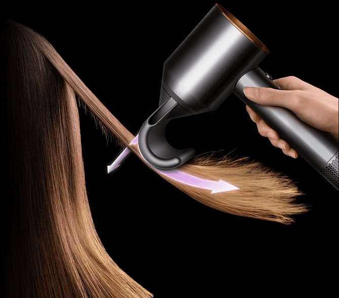 A hand using a Dyson hairdryer, drying hair. Arrow shows the airflow direction.