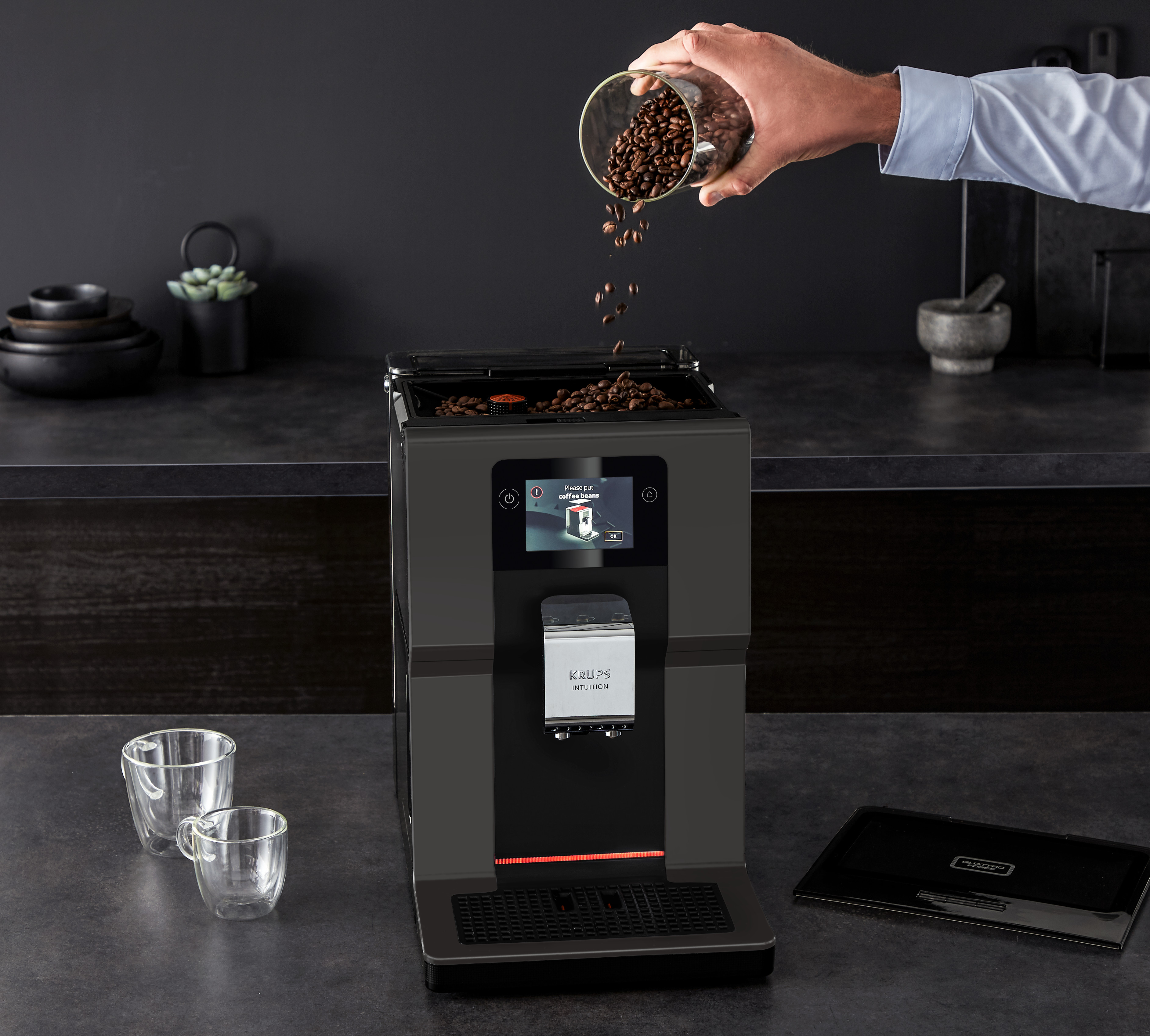 A person pouring coffee beans into a Krups automatic coffee machine on a dark countertop.