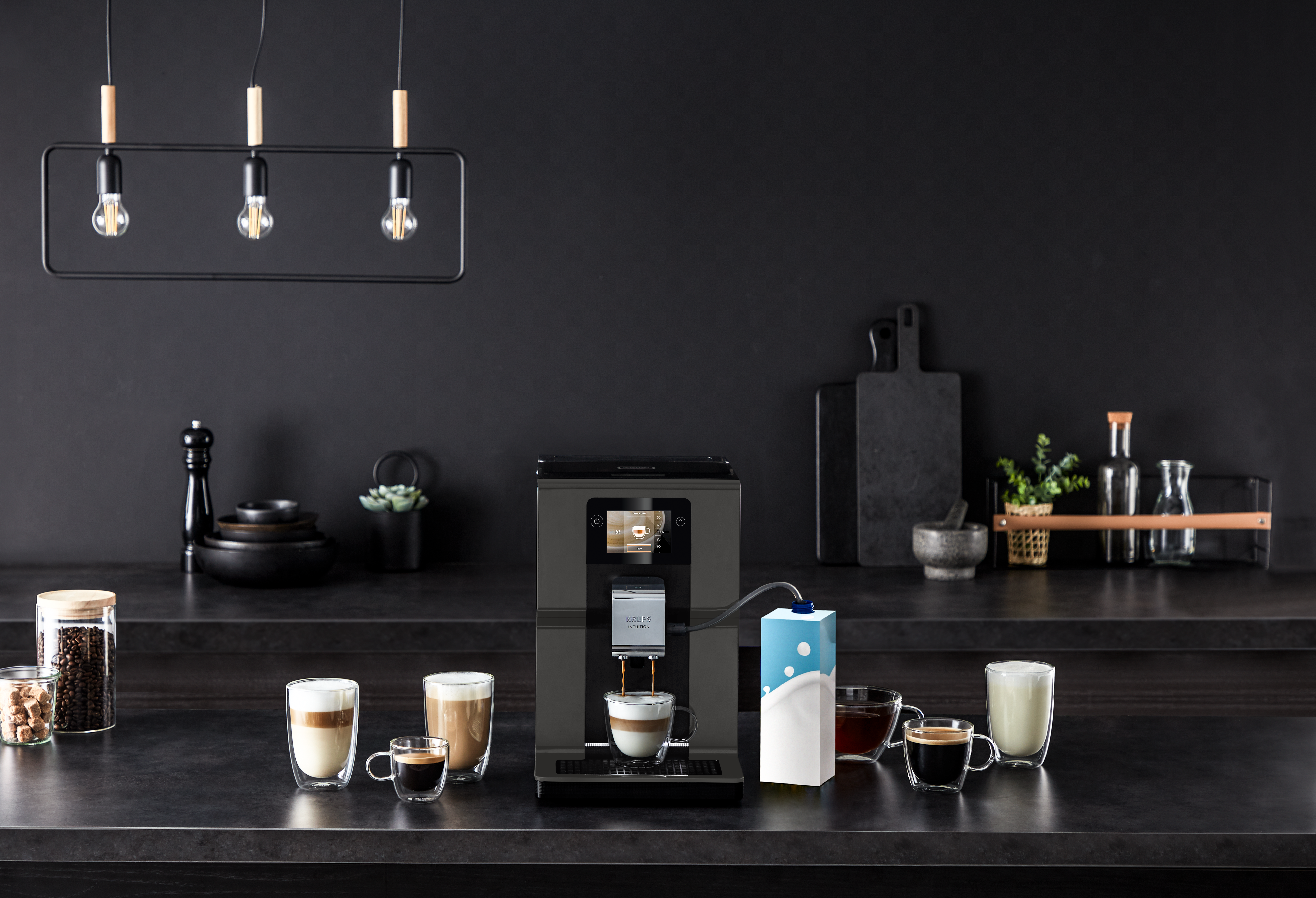 A modern kitchen with a coffee machine, various coffee drinks, and a milk carton. Overhead lights illuminate the scene, dark background.
