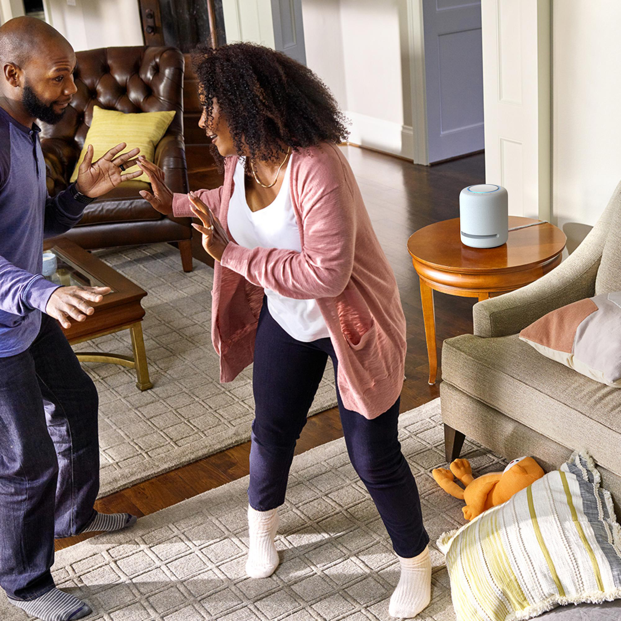 Mann und Frau gestikulieren in einem Wohnzimmer, in der Nähe eines Lautsprechers. Ein Hundespielzeug auf dem Boden.