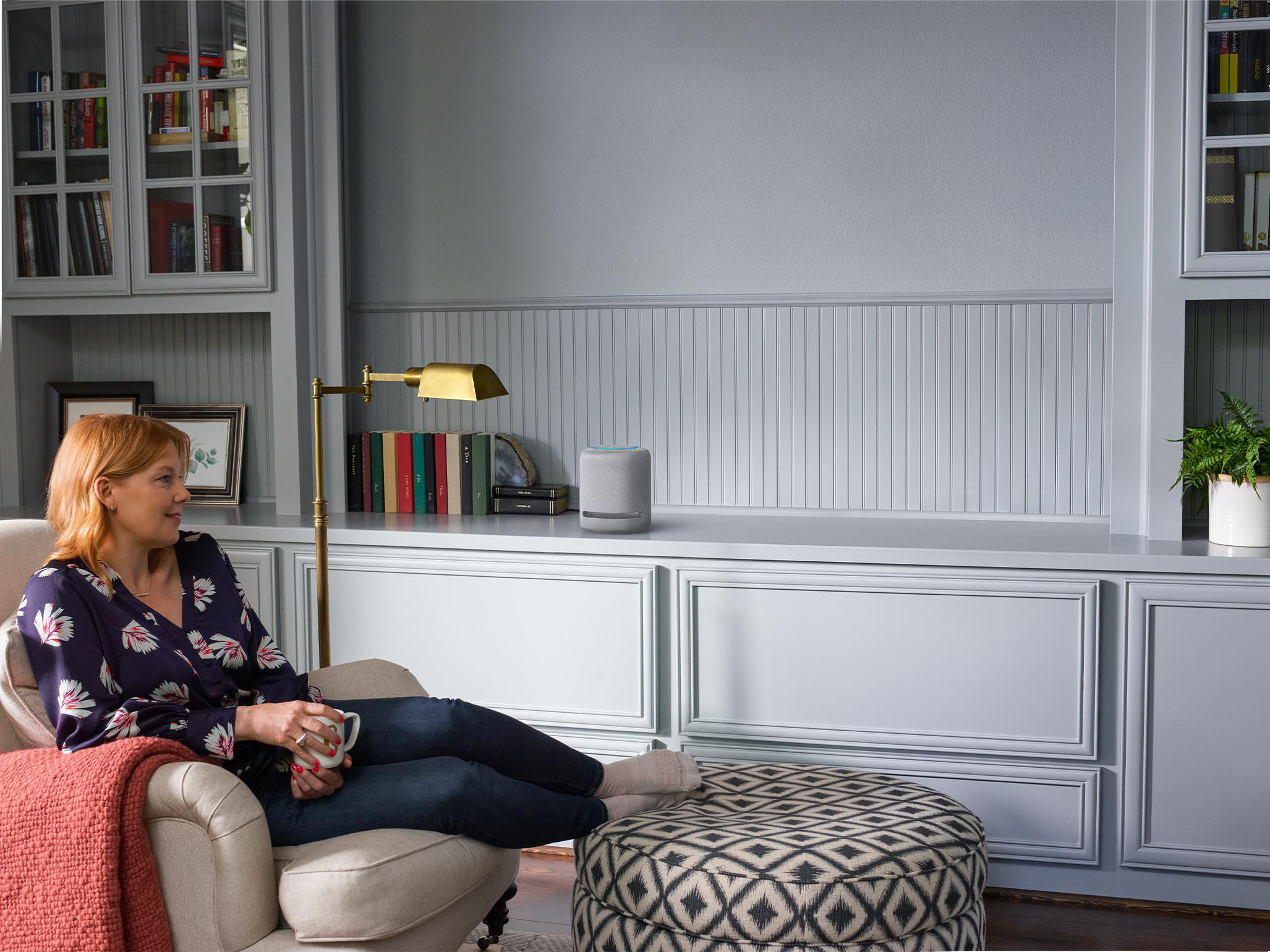 Eine Frau in einem Wohnzimmer sitzt in einem Sessel, in der Nähe einer Lampe und eines Amazon Echo.