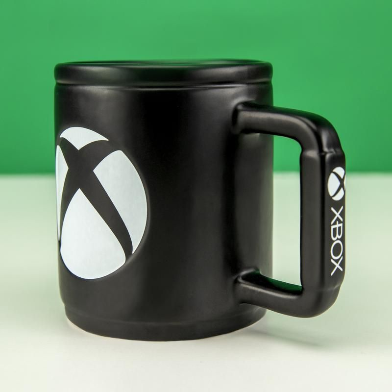 Mug Xbox noir avec logo Xbox blanc. Fond vert et blanc.